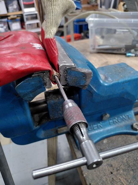 A piece of brass round bar held in a vice wrapped in a red rubber glove
to protect the brass. a hand tap wrench is threaded into the centre of the
part.