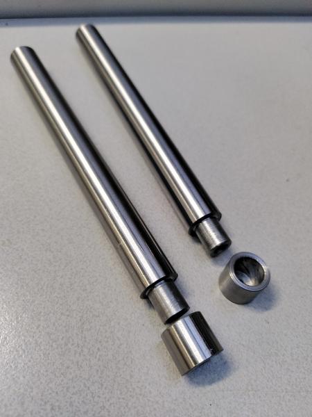 Two bars of polished steel laying on a grey table. One end of each has a
shoulder turned into it. Next to each shoulder there is a cup shaped steel
part. The right bar has the cup sat on it's end so that the inside is
visible. The left hand one is laying coaxial with the bar.