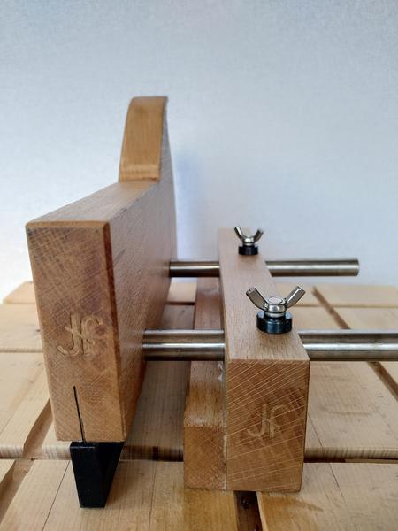 End on view of a wooden kerfing plane. Both the body and fence of the
plane have an ambigram JF makers mark stamped in. The wood has a dark
oiled finish. The arms connecting the body and the fence are shiny steel.
The plane is sat on a dirty beech work bench.