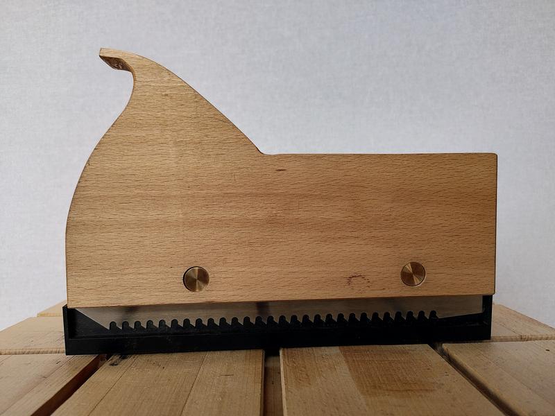 A side on view of a wooden kerfing plane with the blade visible at the
bottom. The blade is framed by a black plastic blade guard.